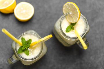 Two glasses of lemonade with straw in jars on dark background. Fresh summer drinks with lemons, top...