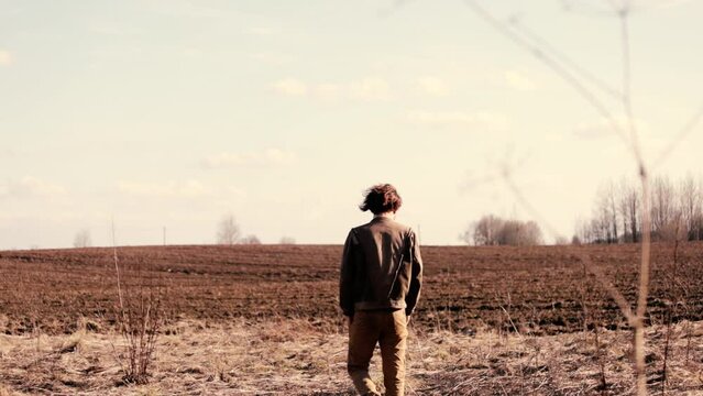 man with long hair in a brown leather jacket walks through a field in depression, existential crisis, midlife crisis