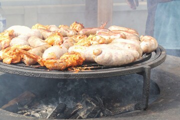 Fried sausages and chicken wings on barbecue grill in the village. Frying meat on open fire. Barbecue party on backyard of country house cabin. Street food festival. Home cooking outdoor. Picnic time