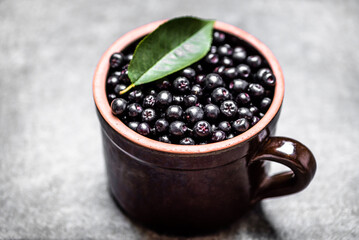 Chokeberry. Bowl of fresh aronia berries in a pot on stone table.