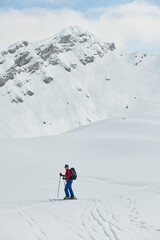 A female skier stands at the snowy summit of a mountain, equipped with professional gear and skis,...