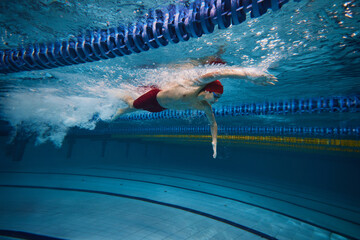 Reaching athletic achievement. Competitive, focused young man, swimmer in motion in pool indoors,...