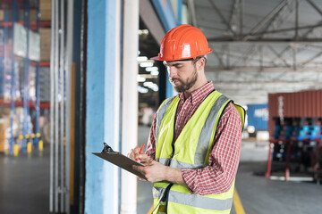 Obraz premium Male warehouse worker holding clipboard during working in storage warehouse. Warehouse worker inspecting quality of products and checking stock inventory