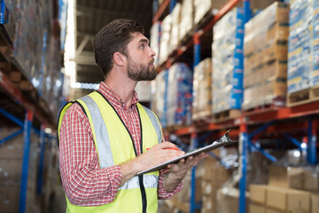 Male warehouse worker holding clipboard during working in storage warehouse. Warehouse worker...