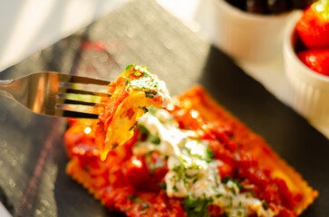 Four cheese filled ravioli in a tomato and basil sauce on the black stone plate - 783087797