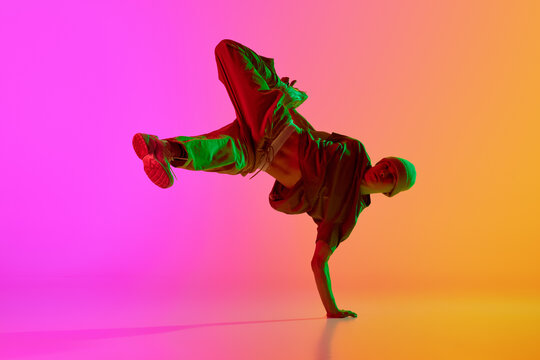 Dynamic photo of young, stylish dressed man dancing in neon light against gradient pink-yellow background. Concept of hobby, sport, creativity, fashion and style, motion, action. Ad