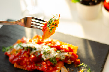 Four cheese filled ravioli in a tomato and basil sauce on the black stone plate - 783088326