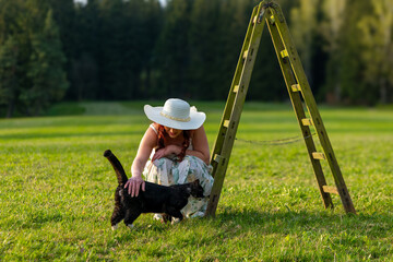 woman on a meadow with a ladder stroking a cat