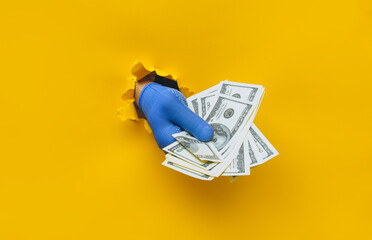 A man's hand in a blue fabric work glove holds dollar bills (money). Torn hole in yellow paper....
