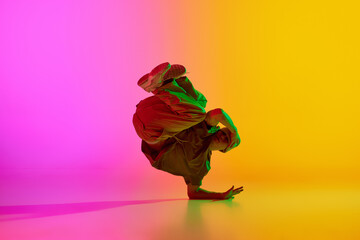 Talented freestyle dancer, young man stands in freeze in neon light against gradient pink-yellow...