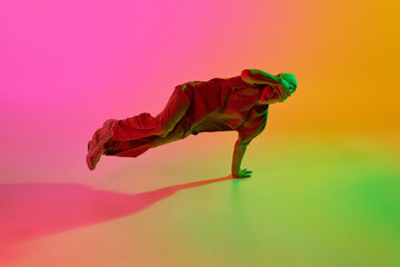 Young athlete man, dressed streetwear dancing hip-hop in motion in neon light against gradient...