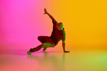 Fototapeta na wymiar Young man, dressed streetwear performing freestyle moves in motion in neon light against gradient pink-yellow background. Concept of art, hobby, sport, creativity, fashion and style, action. Ad