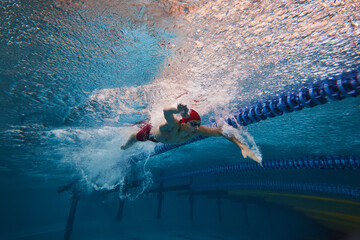 Strength and resilience. Young man, swimmer in red cap and goggles swimming, training in pool...