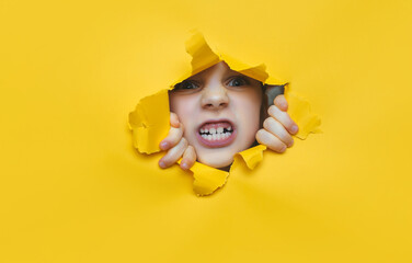 A little girl looks through a torn hole in yellow paper. The concept of anger, fear, fright and shock from what he saw. Unexpected aggression and stress. Copy space.