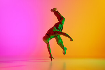 Fototapeta na wymiar Dynamic photo of young, talented man dancing in freestyle in neon light against gradient pink-yellow background. Concept of art, hobby, sport, creativity, fashion and style, action. Ad
