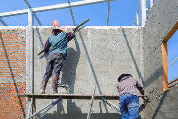 2 Asian builder workers on wooden scaffolding are plastering and polishing concrete wall room in...