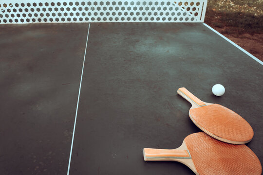 Tavolo da ping pong pubblico all'aperto in un parco con due racchette di legno e una pallina bianca pronte per giocare, concetto di sport, tempo libero e attivit&agrave; ricreativa