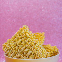 Dry noodles for brewing is in a bowl on a pink shiny sparkled background with bokeh. Close up - 783101306