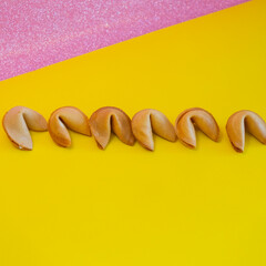 A fortune cookies are laid out in a line on yellow and pink backgrounds, creative concept - 783101540