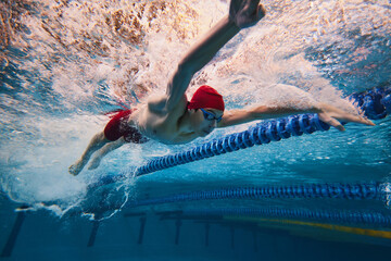 Strength and resilience. Young man, swimmer in red cap and goggles swimming, training in pool...
