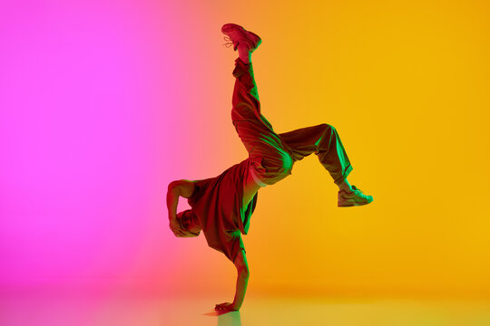 Talented solo artist, male break-dancer performing hip-hop in neon light against gradient pink-yellow background. Concept of art, hobby, sport, creativity, fashion and style, action. Ad