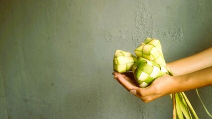 Hand holding ketupat with gray background, special dish served at Eid al Fitr celebration in...