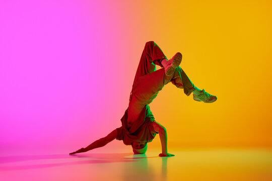 Dynamic photo of break-dancer spinning on head in motion in neon light against gradient pink-yellow background. Concept of art, hobby, sport, creativity, fashion and style, action. Ad