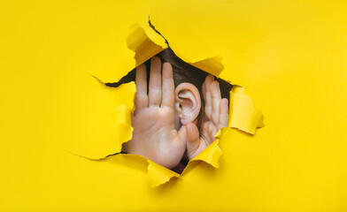 Baby girl's ear and hands close-up. Copy space. Torn paper, yellow background. The concept of...
