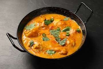 Tasty chicken curry with parsley and pepper on black textured table