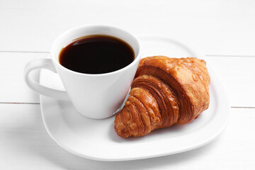 Tasty breakfast. Cup of coffee and croissant on white wooden table