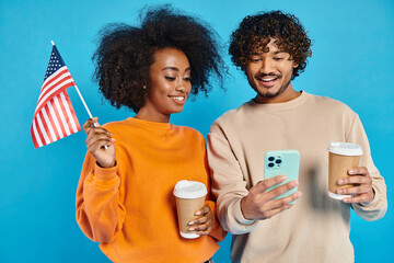 An interracial couple stands holding a cup of coffee and a cell phone, enjoying a moment of...