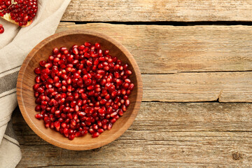 Ripe juicy pomegranate grains in bowl on wooden table, top view. Space for text