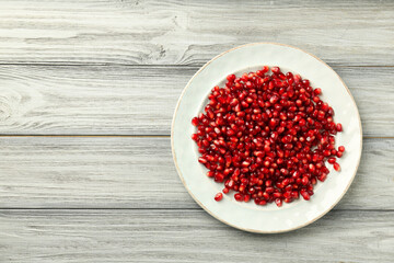 Tasty ripe pomegranate grains on light wooden table, top view. Space for text