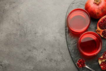 Tasty pomegranate juice in glasses and fresh fruit on grey table, top view. Space for text