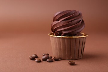 Delicious chocolate cupcake and coffee beans on brown background, closeup. Space for text
