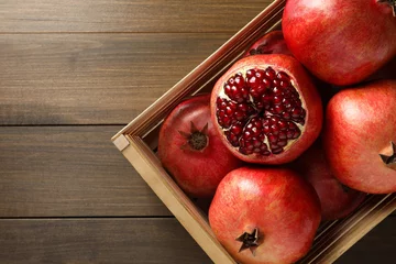 Fotobehang Ripe pomegranates in crate on wooden table, top view. Space for text © New Africa