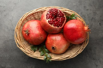 Fotobehang Fresh pomegranates and green leaves in wicker basket on grey table, top view © New Africa