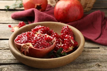 Fotobehang Fresh pomegranates and green leaves on wooden table, closeup © New Africa