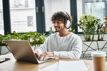 A man of diverse background sits focused in front of a laptop in a modern coworking space.