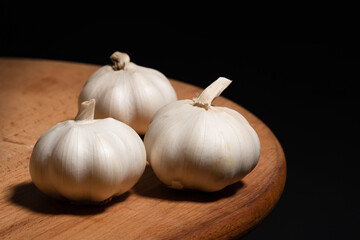 Garlic bulbs on a wooden board on a black background - 783111906