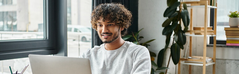 indian man is deeply engaged in work on his laptop computer in a modern coworking space.