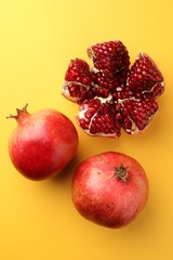 Whole and cut fresh pomegranates on yellow background, flat lay