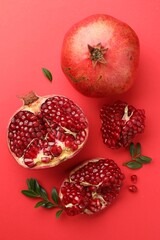 Fresh pomegranates and green leaves on red background, flat lay