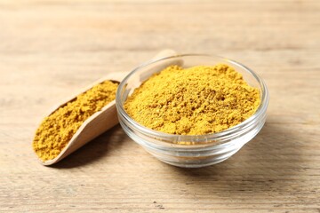 Curry powder in bowl and scoop on wooden table, closeup