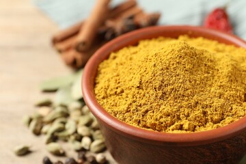 Curry powder in bowl and other spices on wooden table, closeup. Space for text