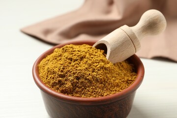 Curry powder in bowl and scoop on white table, closeup