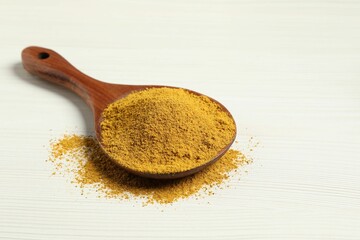 Curry powder in spoon on white wooden table. Space for text