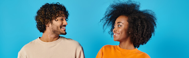 An interracial couple of students standing together casually in a studio against a blue backdrop.