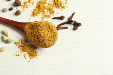 Spoon with dry curry powder and other spices on light wooden table, above view. Space for text