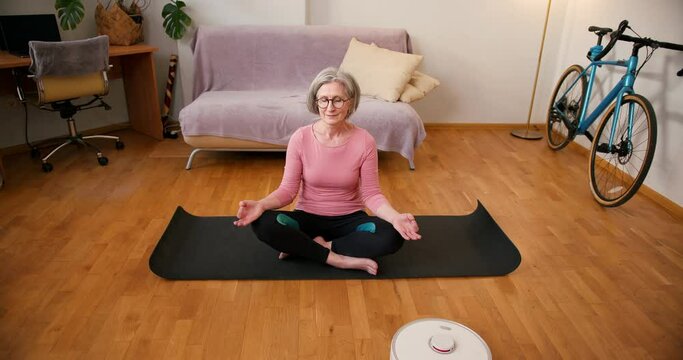 Yoga Online for Senior Mature Woman which Promotes Wellness and Happiness while robot vacuum cleaner making wet cleaning